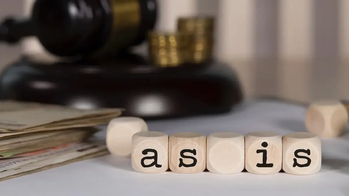 Wooden letter blocks spelling as-is next to a gavel representing as-is clauses in real estate