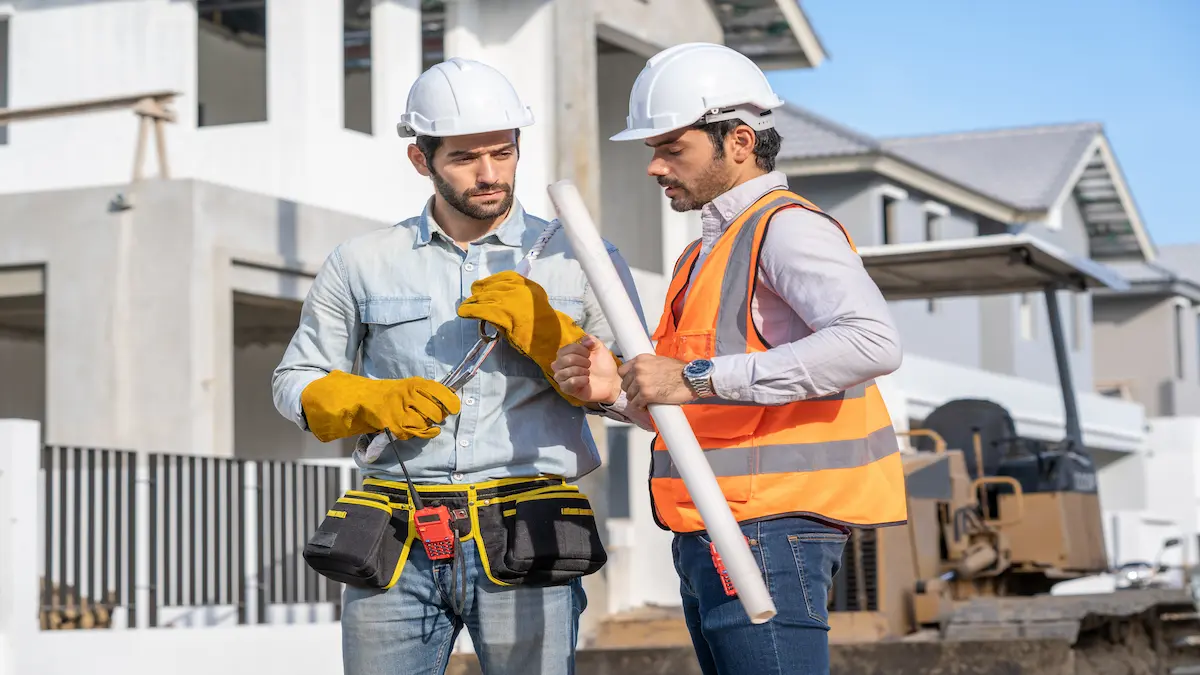 Contractor and project manager reviewing rolled construction plans on a residential job site