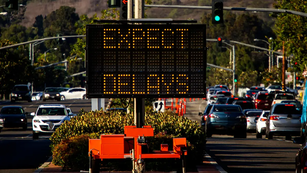 Electronic road sign displaying Expect Delays with traffic backed up on a busy roadway