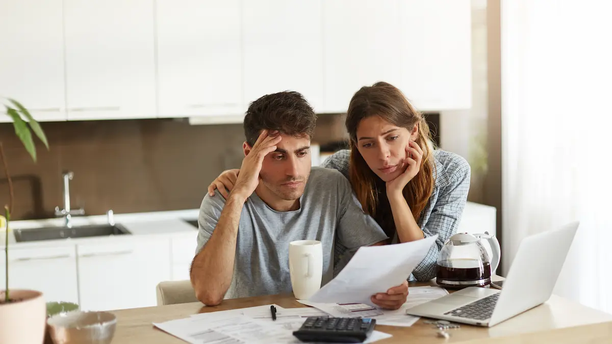 Worried couple reviewing an HOA assessment notice at their kitchen table with paperwork and a laptop